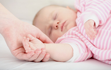 Mum holds by the hand the sleeping baby.