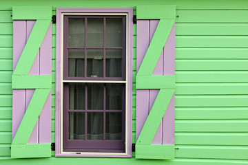 Detail of window with purple and green shutters on wooden house