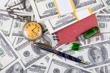 Pocket watch, notebook and pen on a stack of dollars