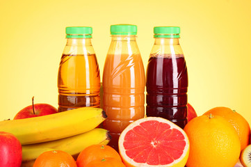 bottles of juice  with ripe fruits on yellow background