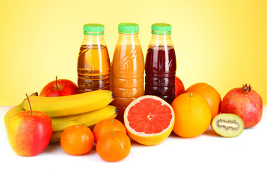 bottles of juice  with ripe fruits on yellow background