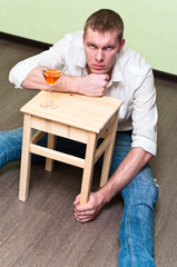 Drunken man sitting on floor with glass of alcohol