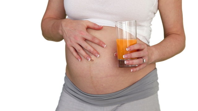 Pregnant woman touching her belly and holding a glass