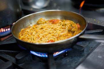 Spaghetti with meatballs in a pan on a gas oven