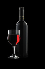 A glass of red wine and a bottle on a black background