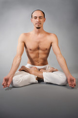 Handsome young man in yoga position. Studio portrait over gray