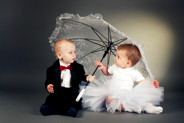 little funny boy and girl sitting under umbrella