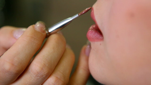 young girl applying lip gloss on her lips