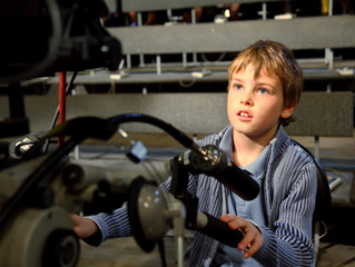 Fototapeta na wymiar Little boy sits on the professional video camera in auditorium