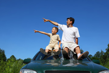 Father with son  sit on  roof of car in  day-time and look aside