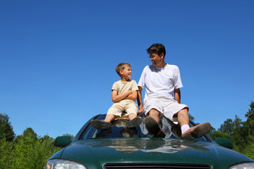 Father with  son sit on  roof of car in  day-time and speak