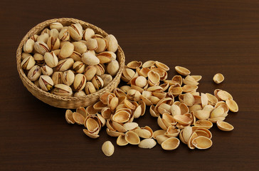Pistachios in interwoven bowl with spilled nutshells on dark woo