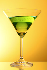 glass with a green alcoholic beverage to a yellow-brown backgrou