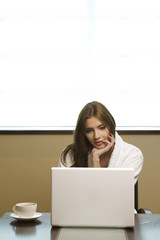 Young woman looks at her laptop computer and drinks her coffee