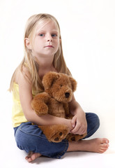Little girl with teddy bear looking sad away from camera.