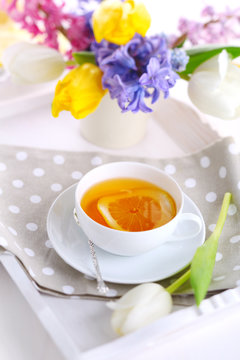 cup of tea with lemon on white tray with spring flowers