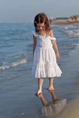 Girl in a white derss walking along a seaside