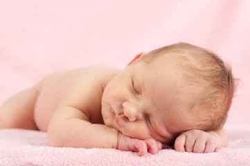 Neugeborenes liegt auf rosa Decke und schläft