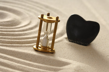 Sanduhr im Sand mit Stein als Herz