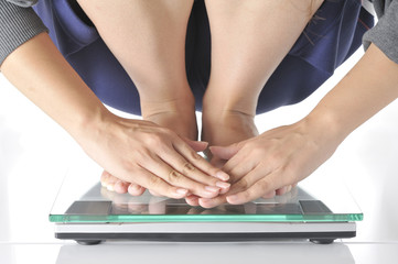 若い情勢が体重計の上で、メモリを隠すように手で覆っている体重測定のシーン