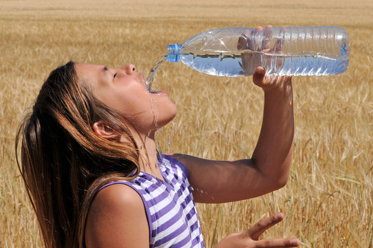 Niña bebiendo agua en un campo de trigo