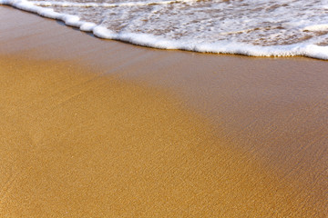 Wet sand on the beach and one wave