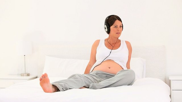 Brunette pregnant woman listening to music in her bed