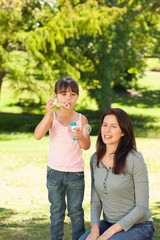 Girl blowing bubbles with her mother in the park