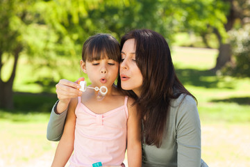 Girl blowing bubbles with her mother in the park