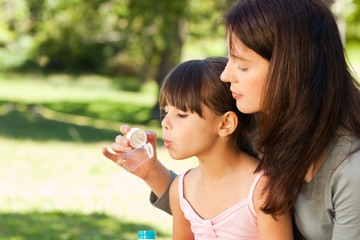 Girl blowing bubbles with her mother in the park