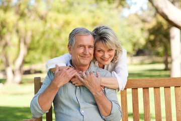 Naklejka premium Senior woman hugging her husband who is on the bench