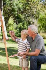 Obraz premium Happy Grandfather and his grandson painting in the garden