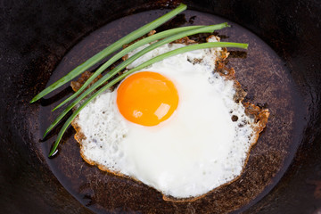 Fried eggs with green onions on a frying pan