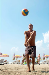 young man playing volleyball on a beach.