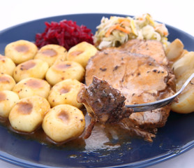 Pork steak and dumplings with salads being eaten with a fork