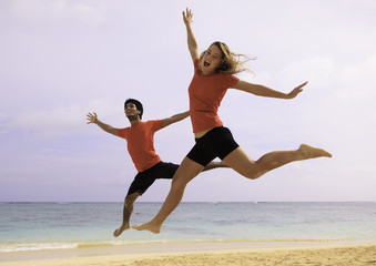 Fototapeta premium young couple jumping in the air at a hawaii beach