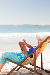 Elderly woman reading a book at the beach
