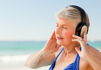 Naklejka premium Senior woman listening to music at the beach