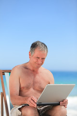 Retired man working on his laptop on the beach