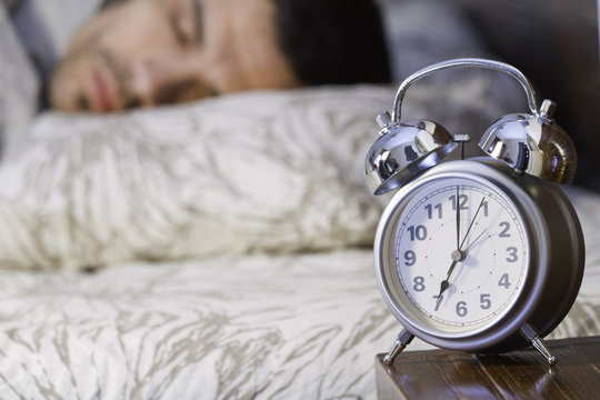 a man sleeping close to a retro alarm clock
