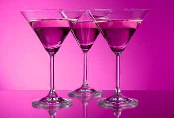 Three empty martini glasses on purple background