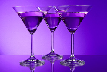 Three empty martini glasses on purple background