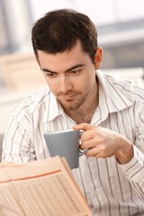 Young man reading news drinking tea in the morning