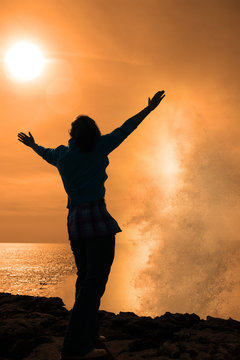 silhouette of lone woman facing a powerful wave in sunshine
