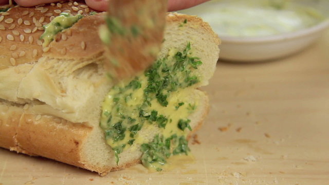 Buttering a sliced bread stick with garlic and herb butter