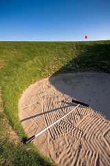 Golf bunker with rake and red flag