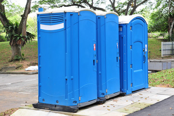 A Row Of Three Blue Color Portable Toilets
