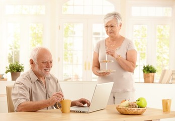 Senior man with computer and coffee in kitchen