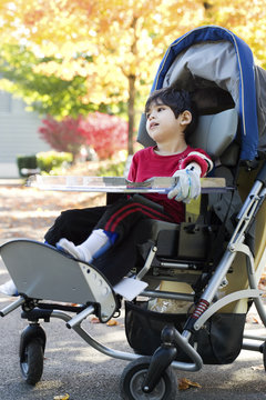 Disabled boy with cerebral palsy in medical stroller  at park