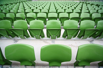 Rows of folded, green, plastic seats in very big, empty stadium.